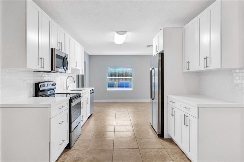 8221 Southwest 3rd Court Pompano Beach, FL 33068 - Photo 2 of 25 a kitchen with stainless steel appliances granite countertop a refrigerator oven a sink dishwasher and white cabinets with wooden floor