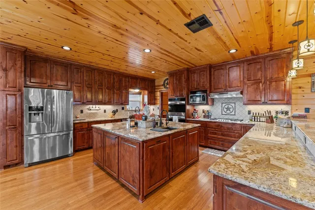 a kitchen with stainless steel appliances granite countertop a stove a refrigerator a sink dishwasher and wooden cabinets with wooden floor