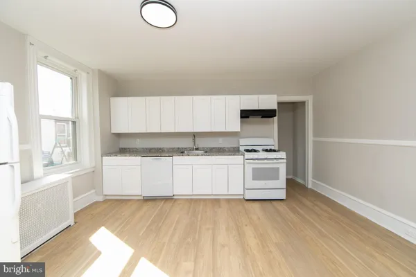 a large white kitchen with granite countertop a stove top oven a sink dishwasher and white cabinets with wooden floor