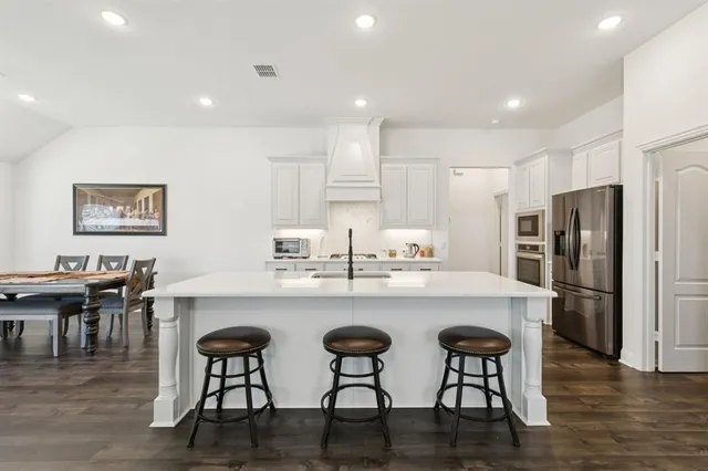 a kitchen with stainless steel appliances granite countertop a dining table chairs refrigerator and cabinets