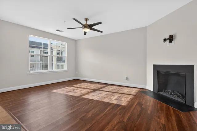 a view of an empty room with wooden floor fireplace and a window