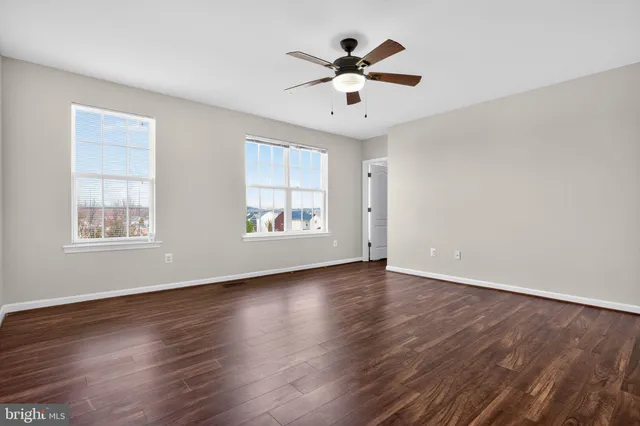 an empty room with wooden floor chandelier fan and windows