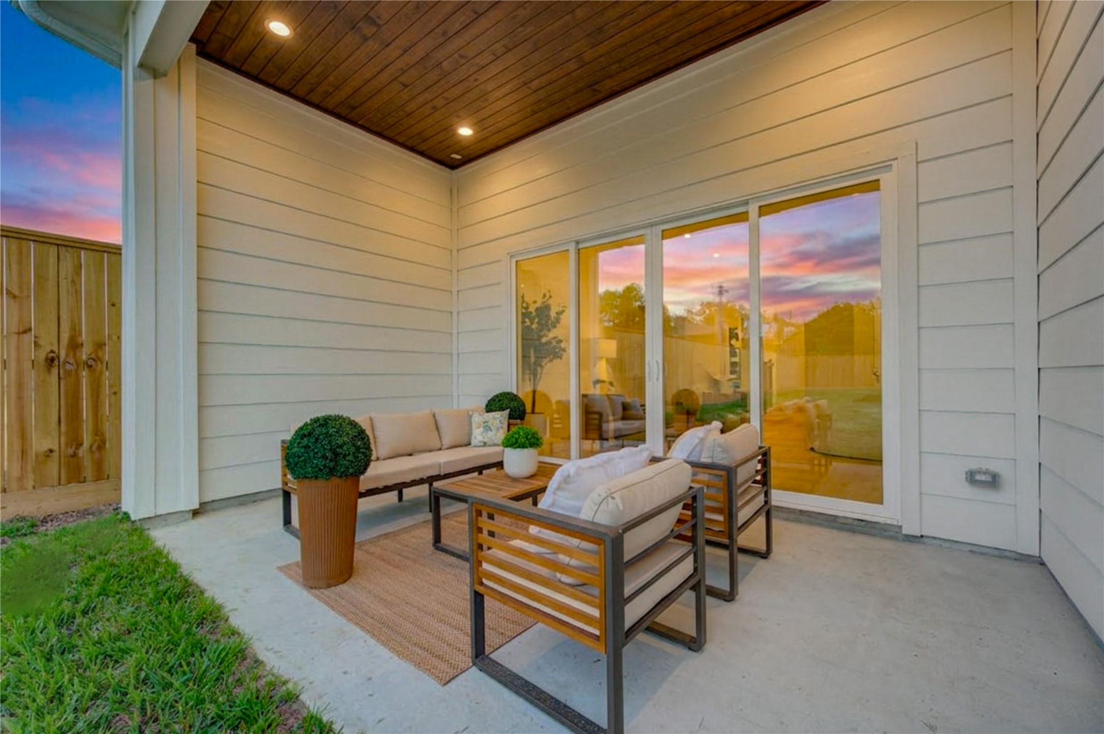 2311 Hollister Road Houston, TX 77080 - Photo 39 of 46 Covered back patio creates a seamless extension of the home’s living space, with expansive glass doors connecting directly to the interior. Warm wood-look ceiling details and recessed lighting elevate the setting, while the adjoining lawn provides additional outdoor space for relaxing, entertaining, or enjoying quiet evenings at home.