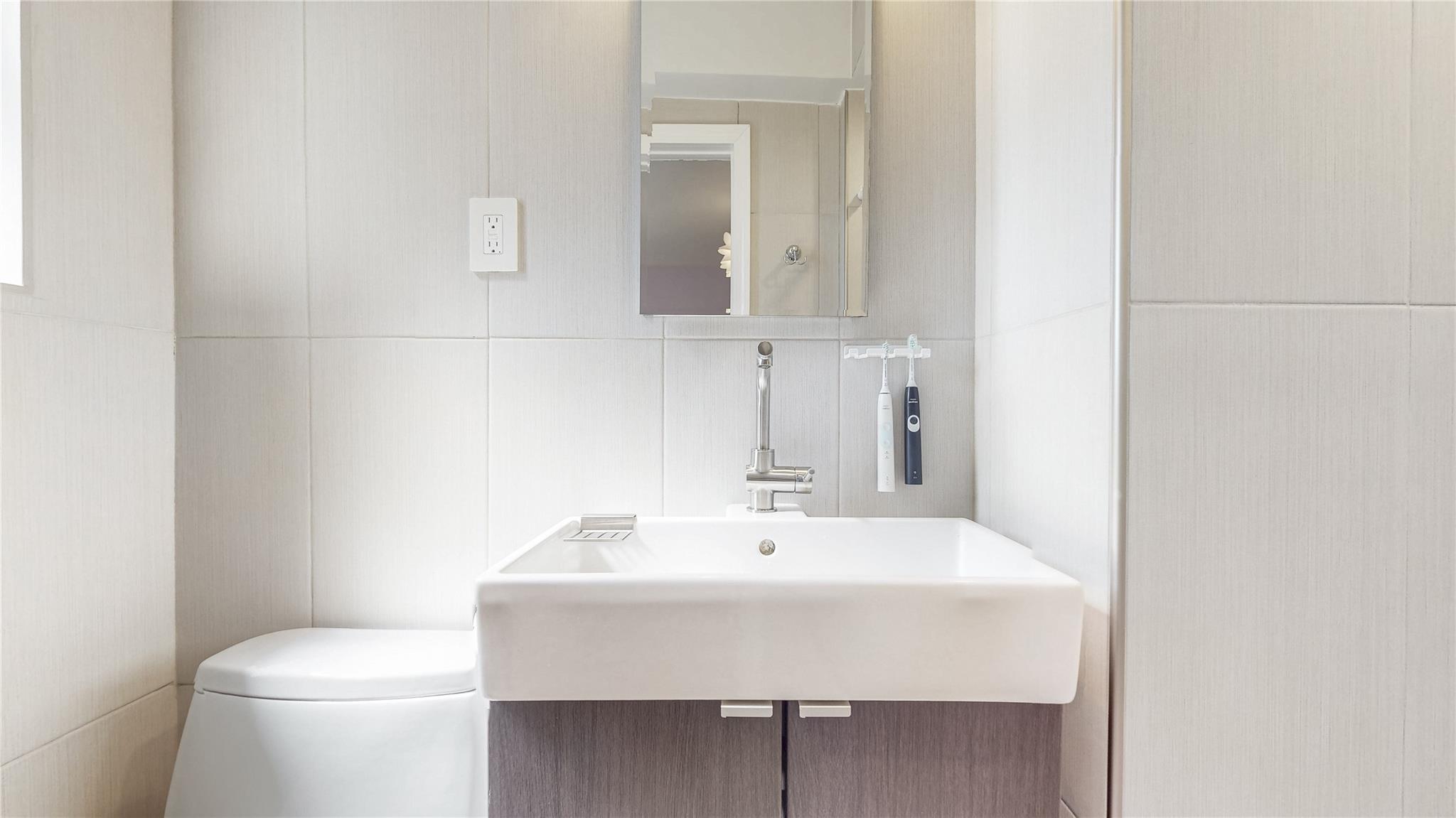 143-50 Hoover Avenue, Unit 507 Queens, NY 11435 - Photo 18 of 24 Half bath with a sink, tasteful backsplash, toilet, and tile walls