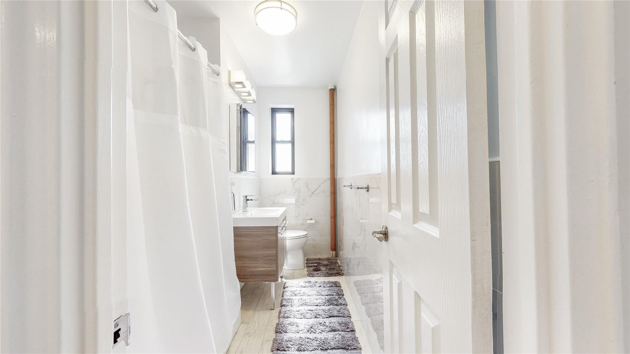 143-50 Hoover Avenue, Unit 507 Queens, NY 11435 - Photo 21 of 24 Bathroom featuring a wainscoted wall, a shower with shower curtain, toilet, vanity, and tile walls
