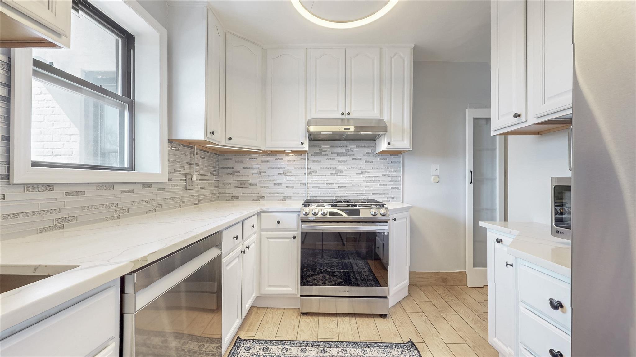 143-50 Hoover Avenue, Unit 507 Queens, NY 11435 - Photo 9 of 24 Kitchen with decorative backsplash, under cabinet range hood, white cabinets, and stainless steel appliances