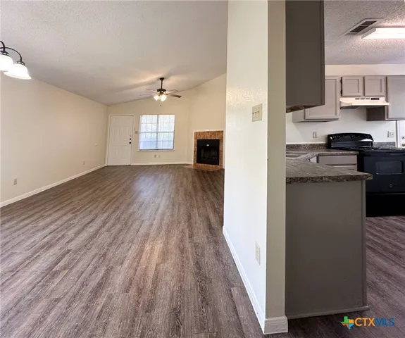 an empty room with wooden floor a ceiling fan and kitchen view