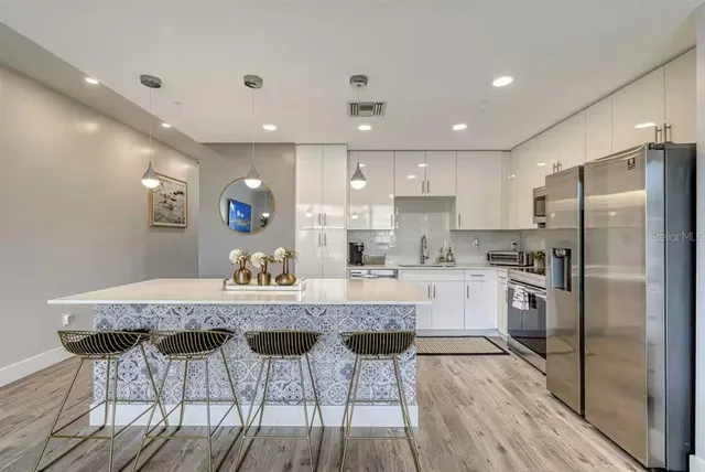 a kitchen with stainless steel appliances granite countertop a dining table chairs refrigerator and microwave