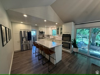 340 Willow Ridge Circle Centerville, UT 84014 - Photo 5 of 32 Vaulted ceiling with recessed lighting, wood-finish flooring, white cabinetry with built-in stainless steel double ovens and refrigerator, kitchen island with stone countertop, and sliding glass patio doors