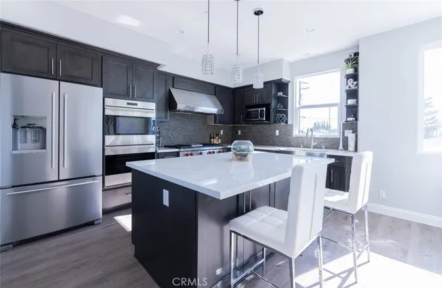 a kitchen with kitchen island granite countertop a sink a microwave a refrigerator and wooden floor