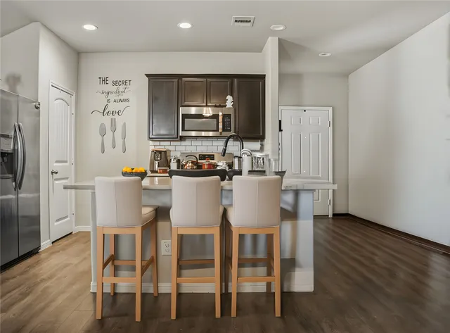 a kitchen with stainless steel appliances a dining table chairs refrigerator and microwave