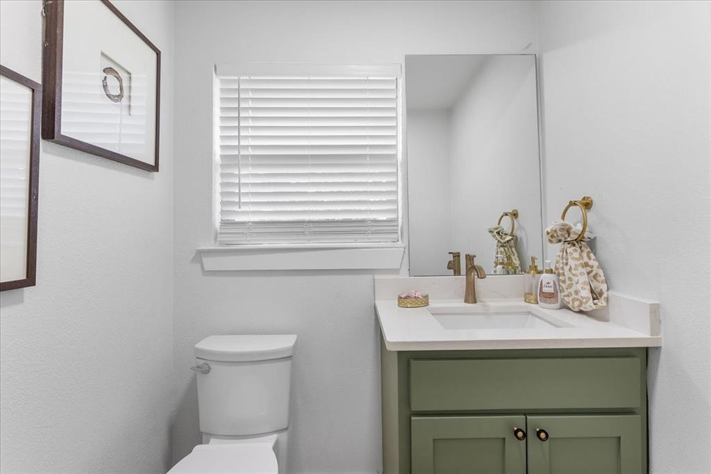 3509 West Sublett Road Arlington, TX 76017 - Photo 31 of 39 Half Bathroom near kitchen with white toilet, vanity with sage green cabinetry, integrated sink, and bronze-finish faucet, accompanied by a wall-mounted mirror