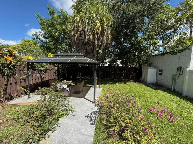 a view of backyard with table and chairs under an umbrella with large trees