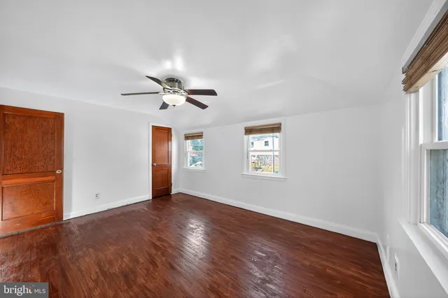 an empty room with wooden floor chandelier fan and windows