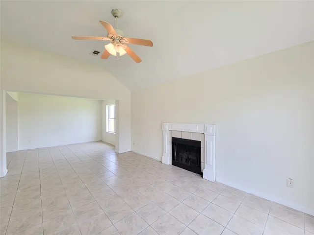 a view of an empty room with chandelier fan and fire place
