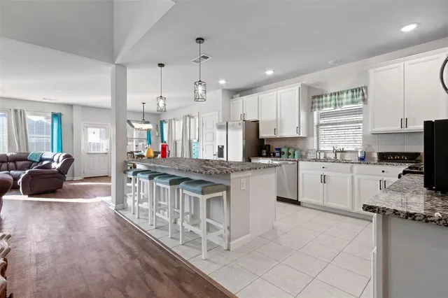 a kitchen with stainless steel appliances kitchen island granite countertop a stove a sink a refrigerator and white cabinets