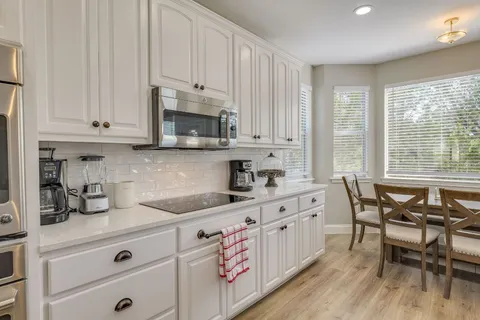 a kitchen with stainless steel appliances granite countertop a stove a sink dishwasher and white cabinets with wooden floor