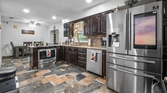 a kitchen with stainless steel appliances granite countertop a refrigerator a sink dishwasher a stove with wooden cabinets and floor