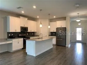 a kitchen with stainless steel appliances kitchen island granite countertop a stove a sink a refrigerator and white cabinets with wooden floor