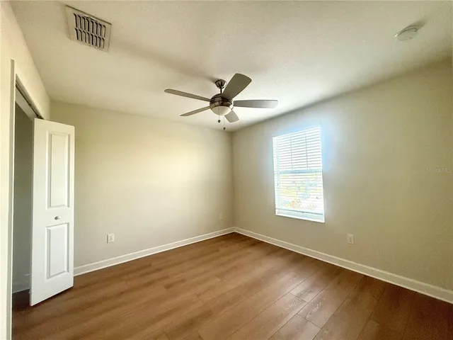 an empty room with wooden floor fan and windows