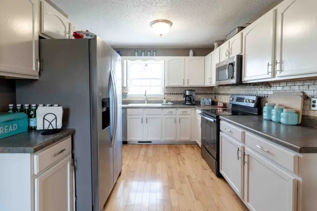 a kitchen with stainless steel appliances granite countertop a refrigerator a sink dishwasher and white cabinets with wooden floor