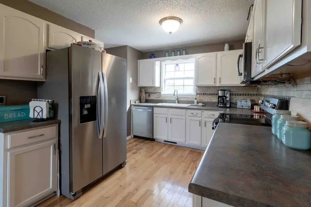 a kitchen with stainless steel appliances granite countertop a refrigerator a sink dishwasher a stove and white countertops with wooden floor