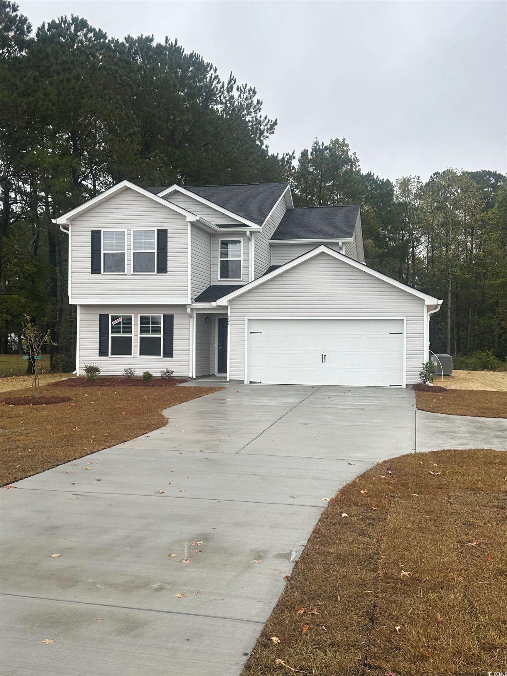 View of front of house featuring driveway, view of wooded area, and an attached garage