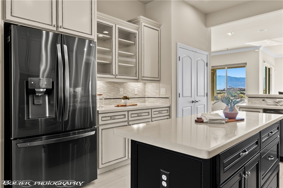 1348 Basin View Mesquite, NV 89034 - Photo 20 of 70 Kitchen featuring dark cabinetry, stainless steel refrigerator with ice dispenser, glass insert cabinets, tasteful backsplash, and light stone countertops