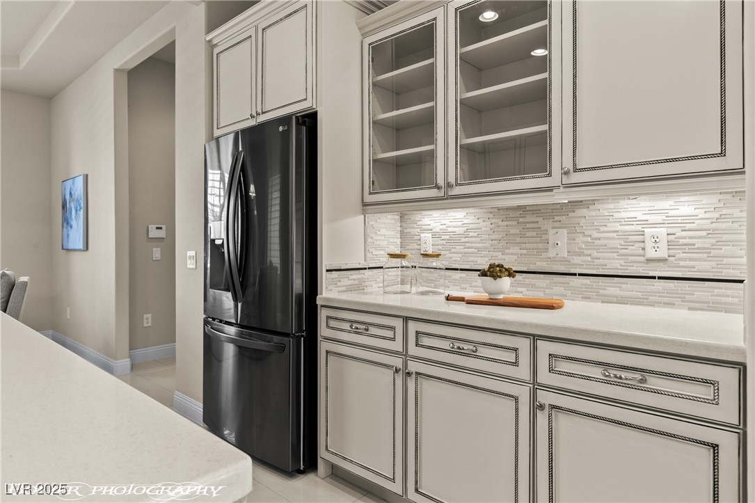 1348 Basin View Mesquite, NV 89034 - Photo 21 of 70 Kitchen with black fridge, tasteful backsplash, glass insert cabinets, light stone countertops, and light tile patterned flooring