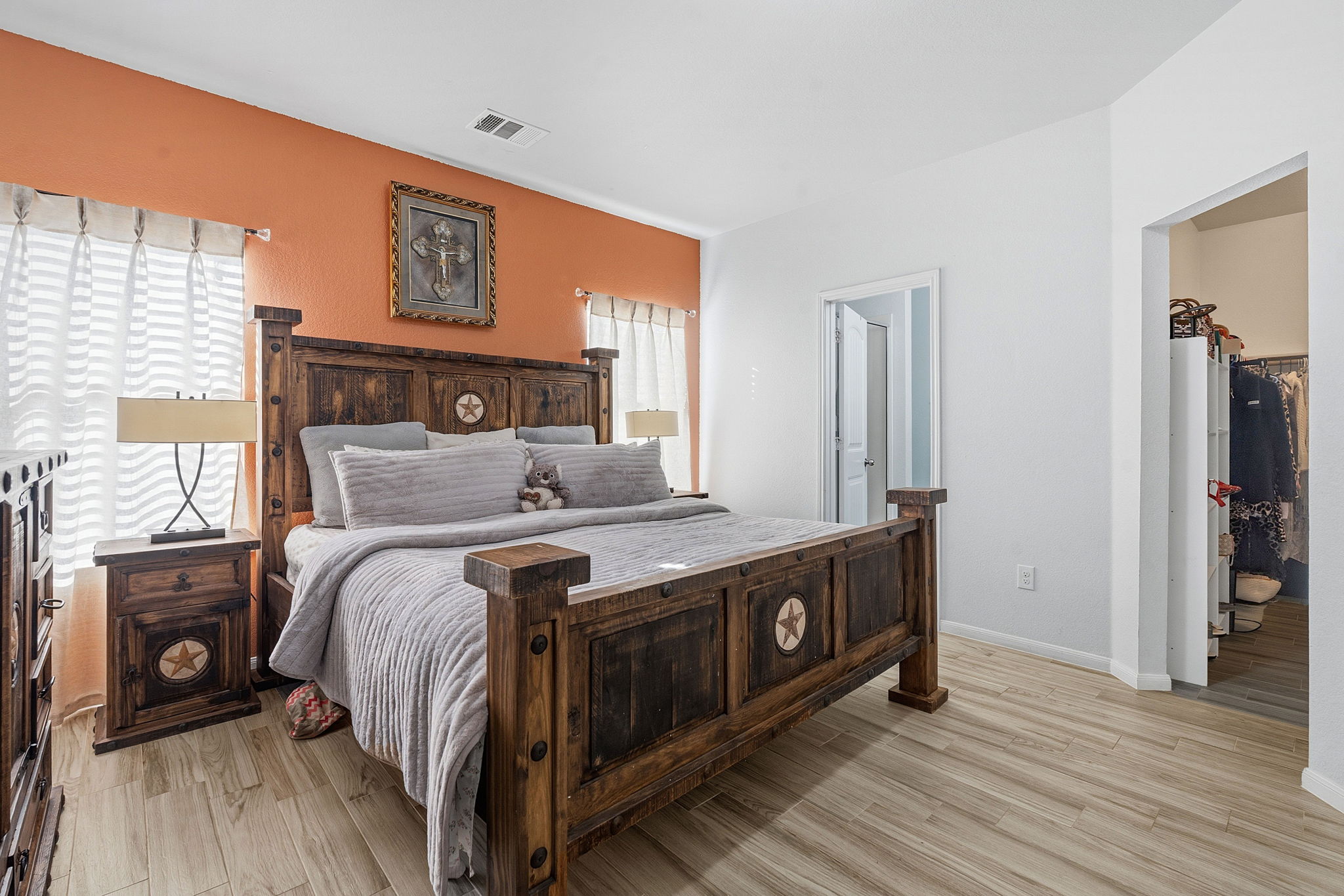 15101 Shell Bark Cove Austin, TX 78724 - Photo 21 of 26 Spacious bedroom featuring wood-finish flooring, a warm accent wall, white wall finishes, and a doorway leading to an additional space