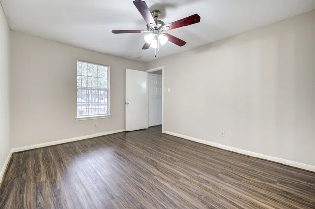 an empty room with wooden floor chandelier fan and windows