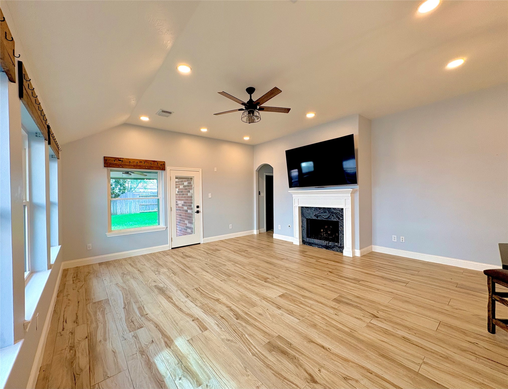 15410 Redbud Berry Way Cypress, TX 77433 - Photo 18 of 49 This spacious living room features a high ceiling with recessed lighting and a ceiling fan, a fireplace with a mounted TV above, and large windows providing natural light. The room has wood-like flooring and access to a backyard through a door with a window.
