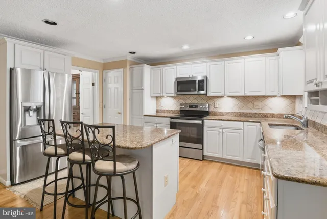 a kitchen with stainless steel appliances granite countertop a stove top oven a sink a refrigerator with a dining table and chairs