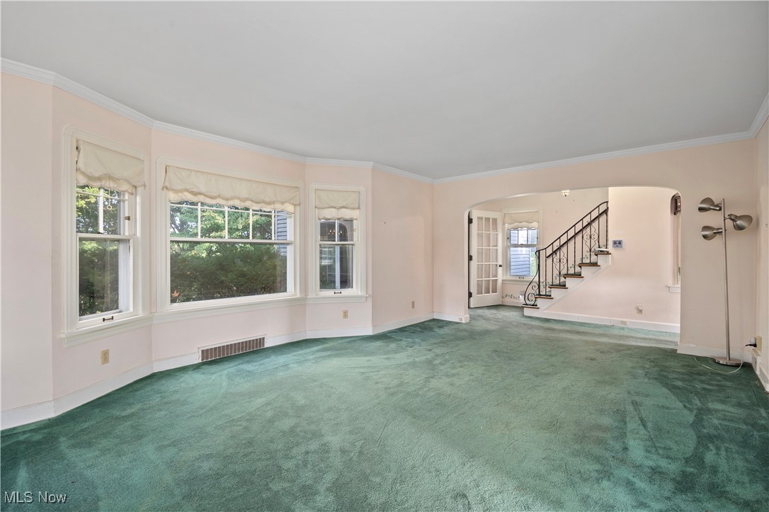 Unfurnished living room with arched walkways, stairway, ornamental molding, and carpet