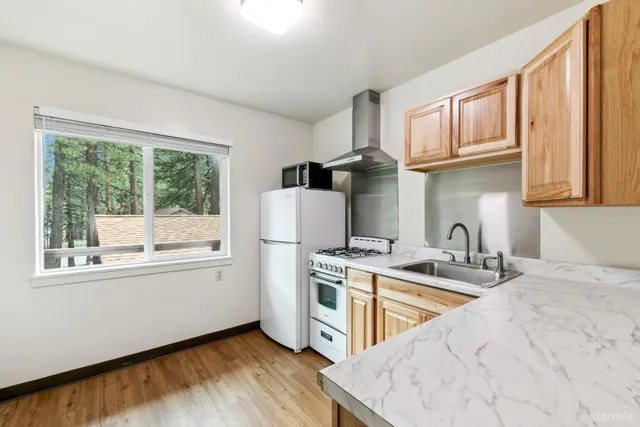 a kitchen with stainless steel appliances granite countertop a stove a sink a refrigerator and white cabinets with wooden floor