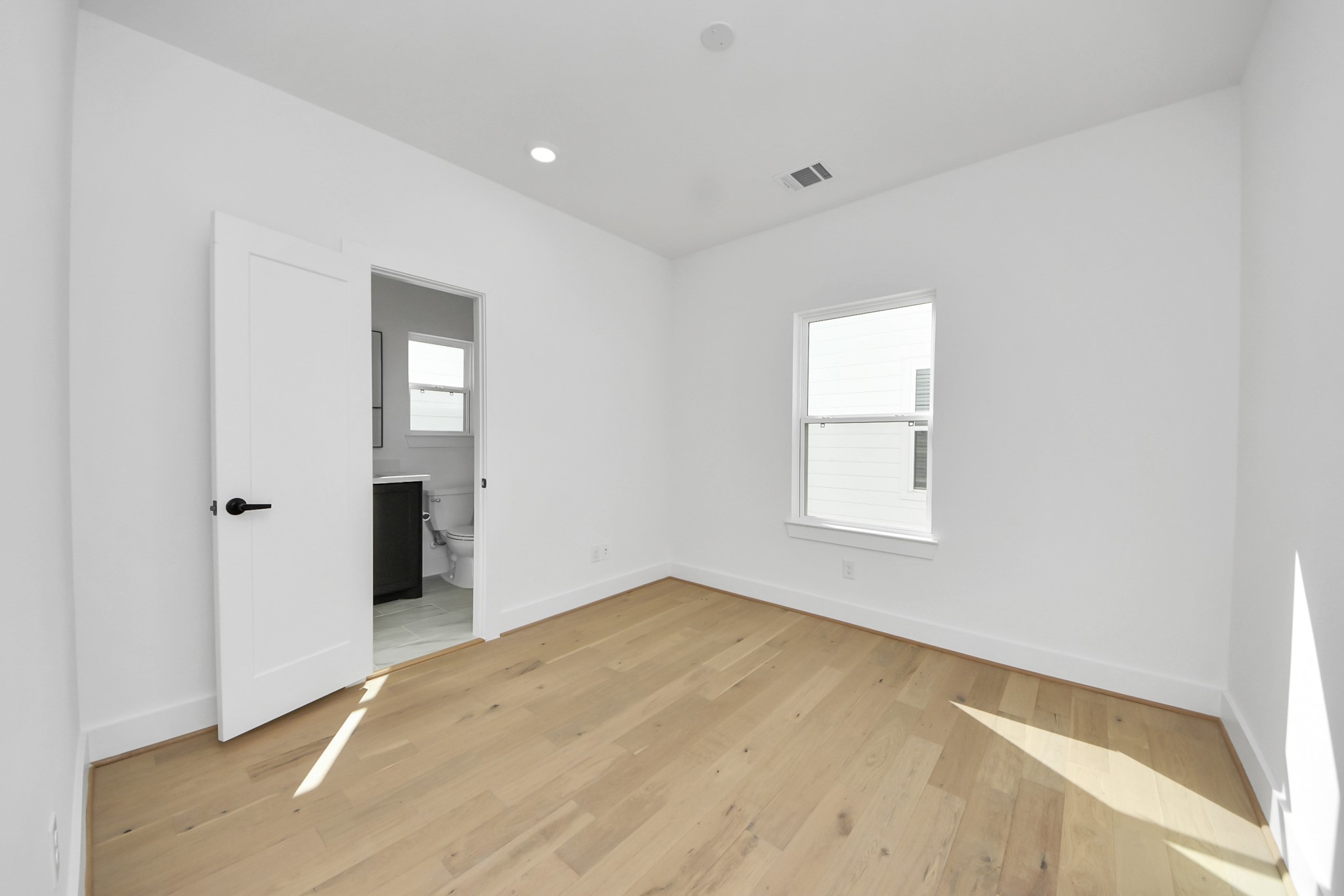 723 Marcella Street, Unit B Houston, TX 77091 - Photo 15 of 22 This bright, minimalist bedroom features light hardwood floors and a large window that lets in natural light. It includes an en-suite bathroom with modern fixtures, adding convenience and privacy.
