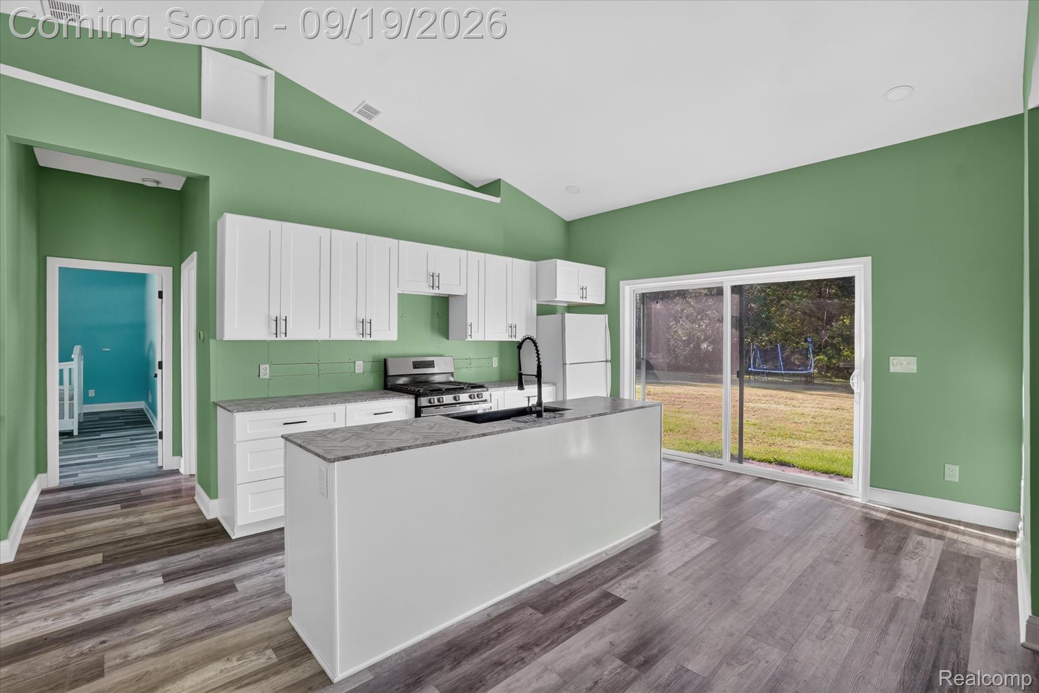 10215 West Mount Morris Road Flushing, MI 48433 - Photo 16 of 58 Vaulted ceiling, wood-finish flooring, white cabinetry, island with countertop, and sliding glass door