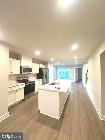 a large white kitchen with kitchen island a stove a sink a refrigerator and white cabinets with wooden floor