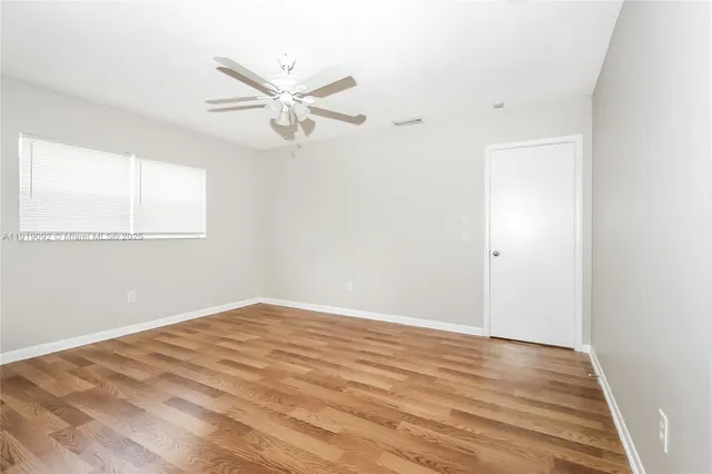 an empty room with wooden floor fan and windows