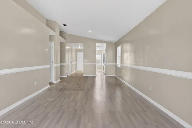 a view of an empty room with wooden floor kitchen view and a window