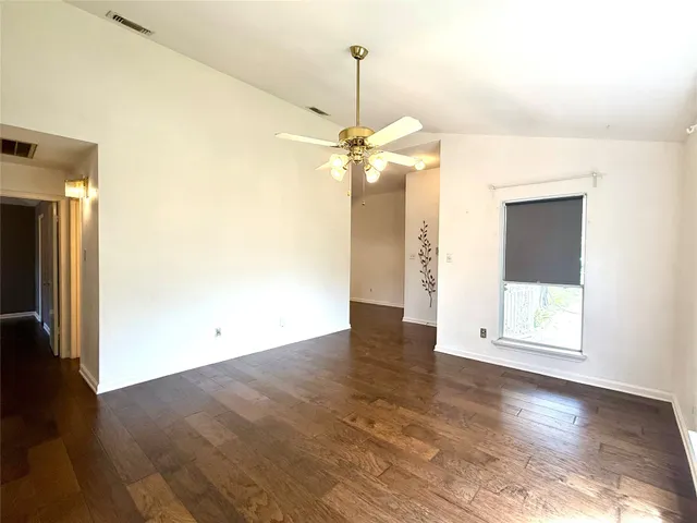 an empty room with wooden floor fan and windows