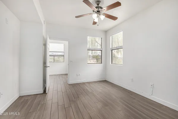 an empty room with wooden floor chandelier fan and windows