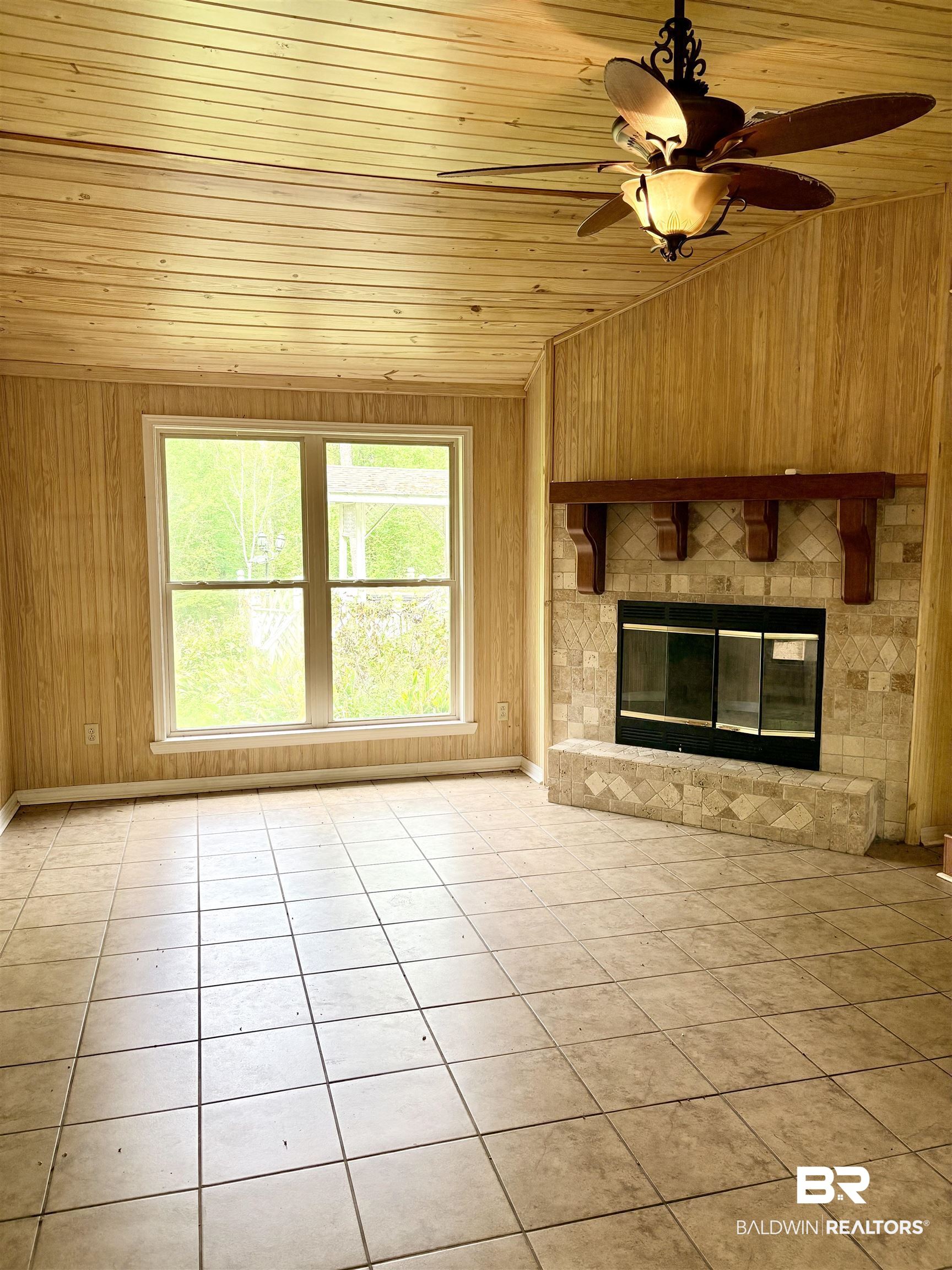 1018 Bates Road Evergreen, AL 36401 - Photo 3 of 21 Unfurnished living room with ceiling fan, wooden walls, a glass covered fireplace, light tile patterned floors, and a vaulted wooden ceiling