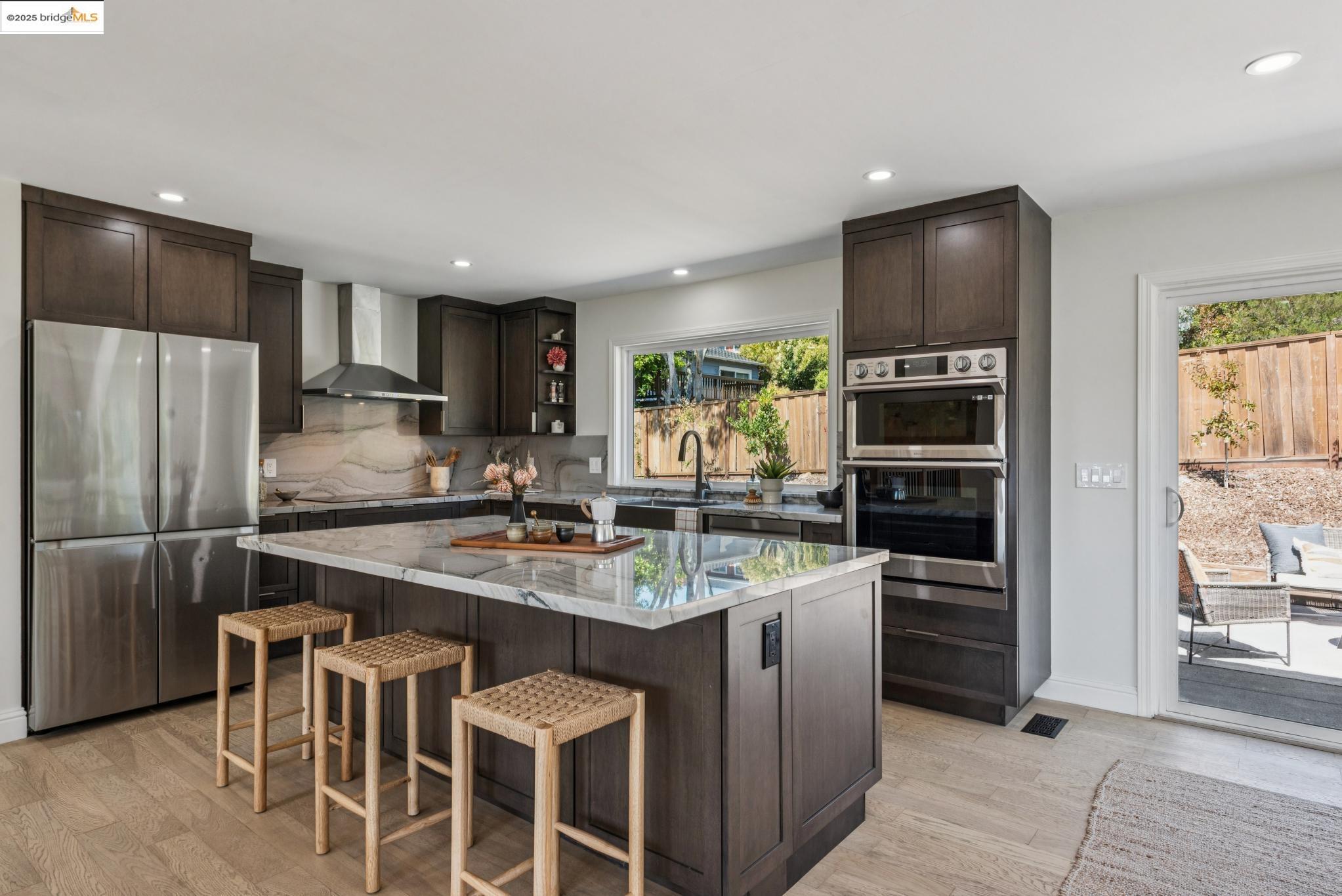 9 Yarmouth Court Oakland, CA 94619 - Photo 16 of 54 Kitchen featuring dark brown cabinets, appliances with stainless steel finishes, recessed lighting, light stone countertops, and wall chimney exhaust hood