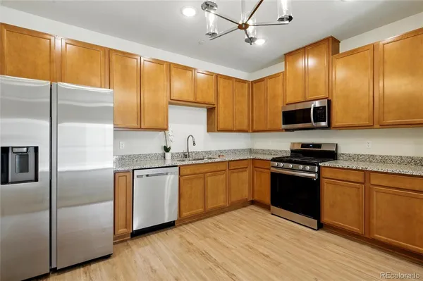 a kitchen with stainless steel appliances granite countertop a stove a sink dishwasher a refrigerator and a microwave oven with wooden floor