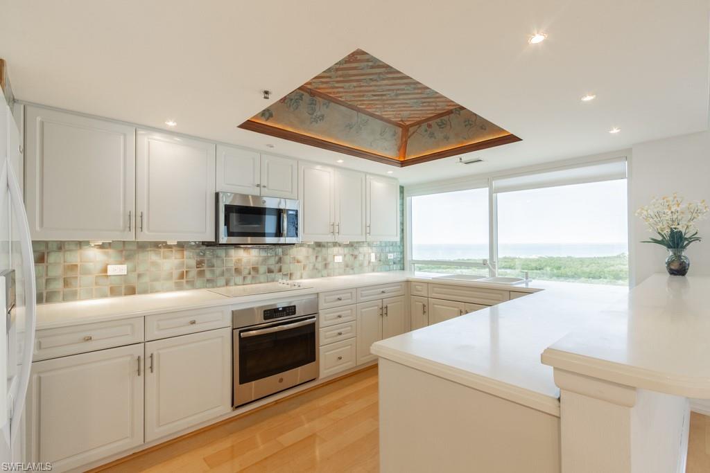 6825 Grenadier Boulevard, Unit 1505 Naples, FL 34108 - Photo 13 of 35 a kitchen with a sink dishwasher a stove and white cabinets with wooden floor