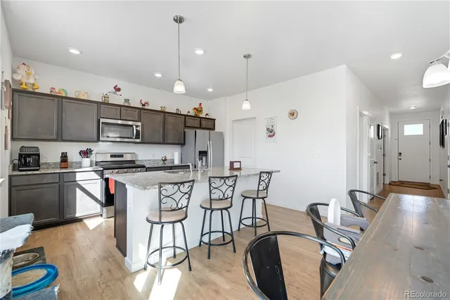 a kitchen with stainless steel appliances granite countertop a stove top oven a sink a dining table and chairs with wooden floor