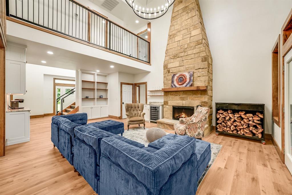 1037 Harrison Road Denison, TX 75021 - Photo 3 of 39 Two-story living area featuring a stone fireplace with a wood mantle, wood-finish flooring, a metal-railed second-story balcony, built-in shelving, and recessed lighting