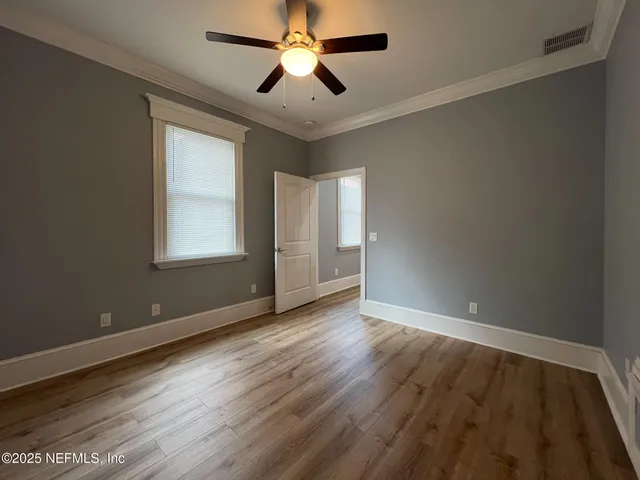 an empty room with wooden floor ceiling fan and windows