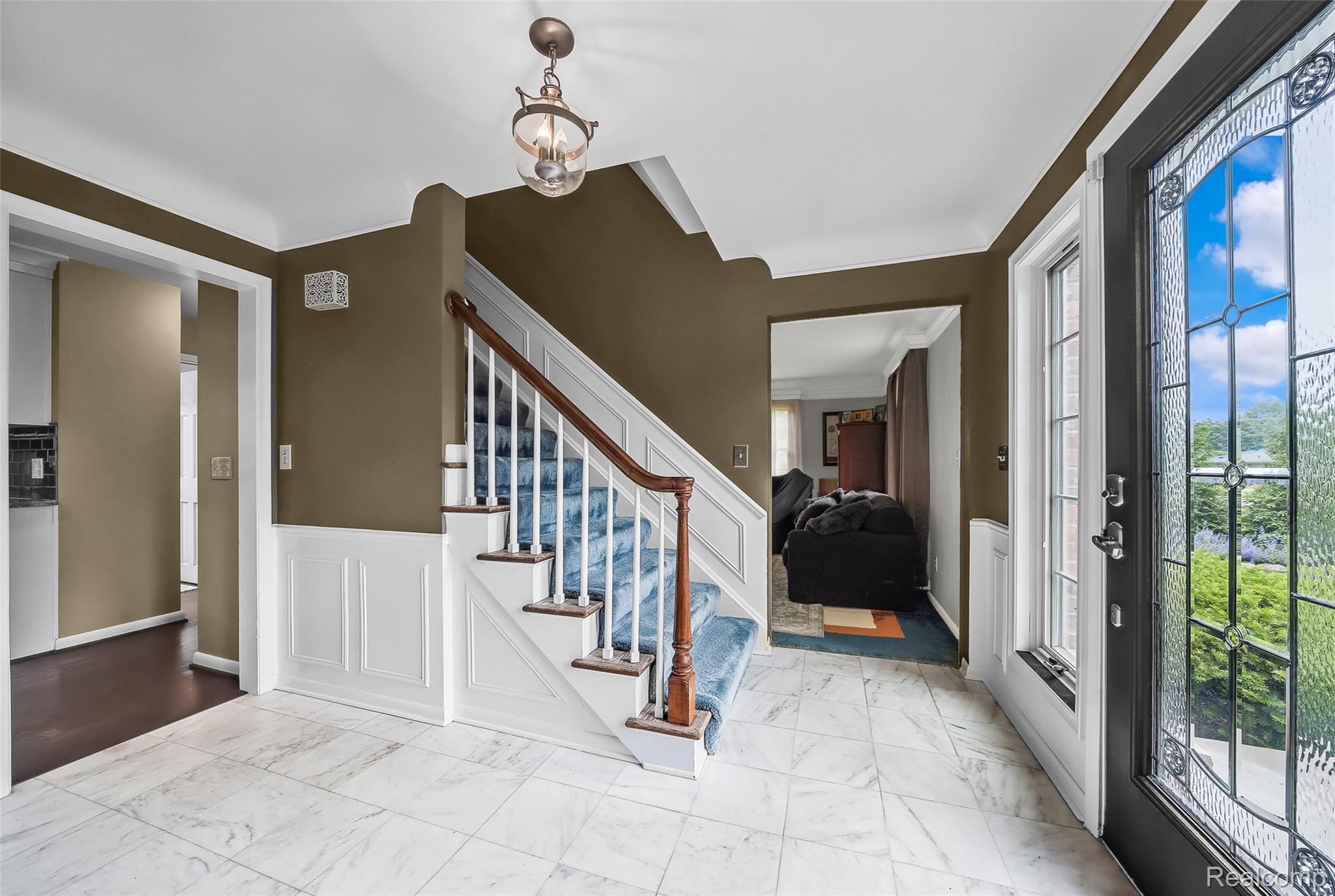 Entrance foyer featuring wainscoting, a decorative wall, marble finish flooring, stairs, and a chandelier